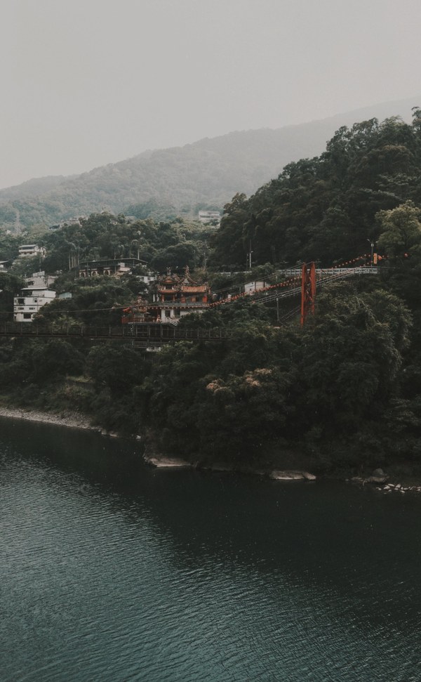 Suspension bridge leading to a hillside temple above a lake