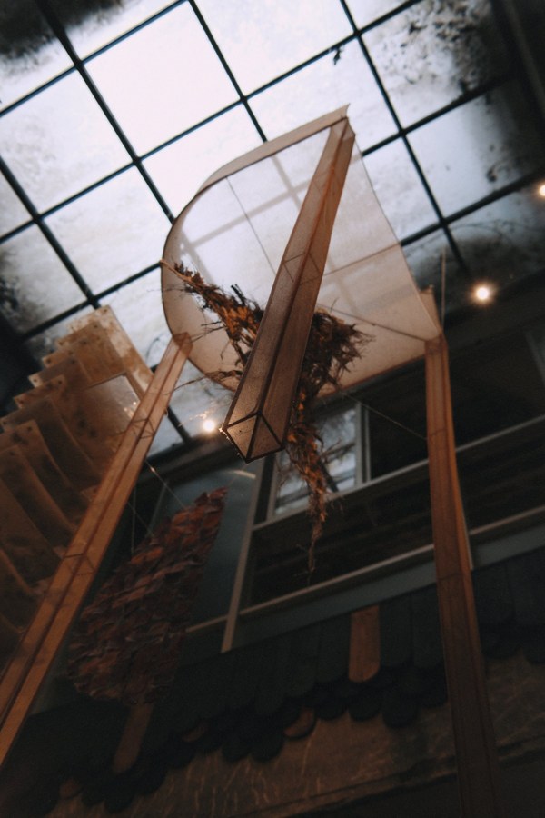 Sculptural wing-like installation of wood and dried branches beneath a glass skylight