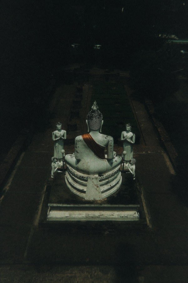 Buddha statue viewed from behind, flanked by two standing monk statues, at dusk
