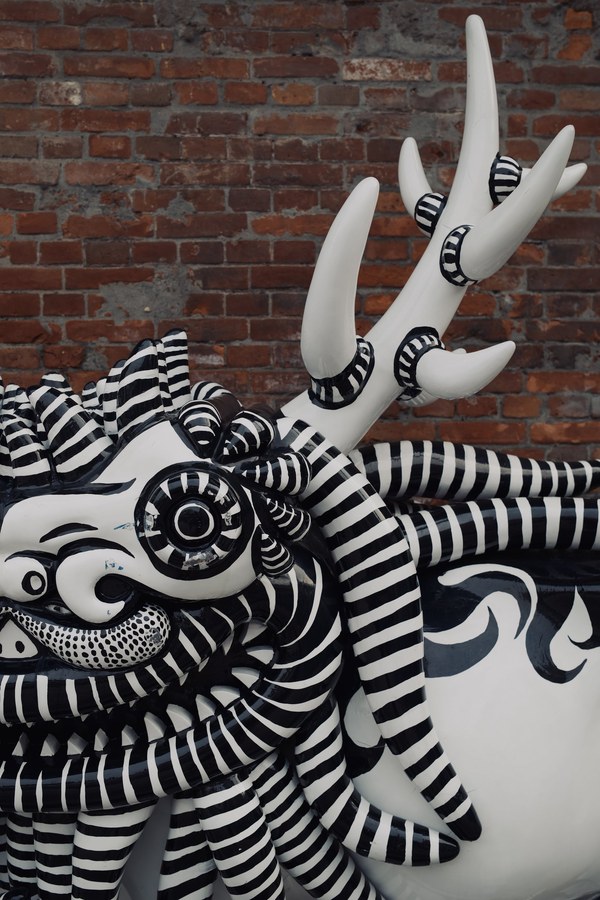 Black and white striped sculptural creature against a brick wall